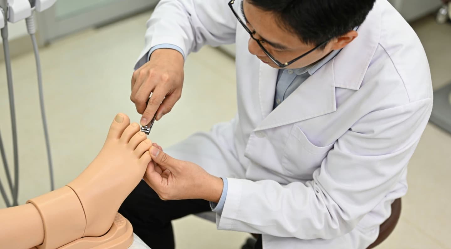 Asian dermatologist demonstrating proper toenail trimming technique on a foot model in clinic.